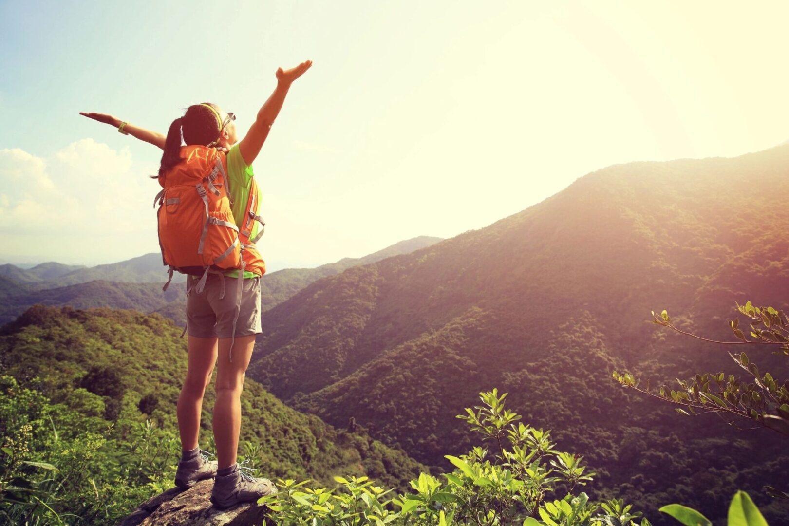 Cheering woman hiker open arms at mountain peak cliff